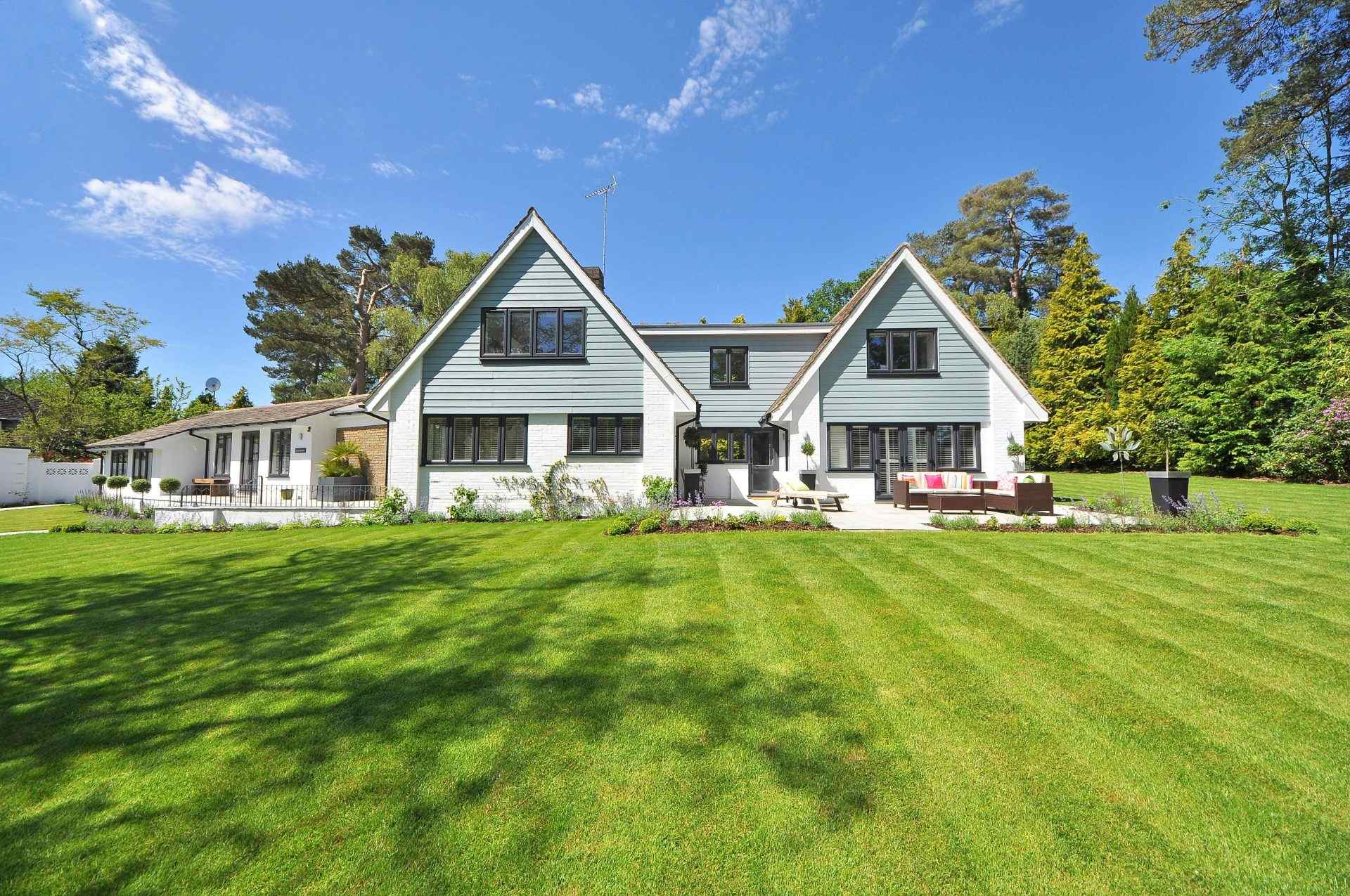 Außenansicht eines modernen Einfamilienhauses mit großem Rasen und Garten unter einem klaren blauen Himmel.